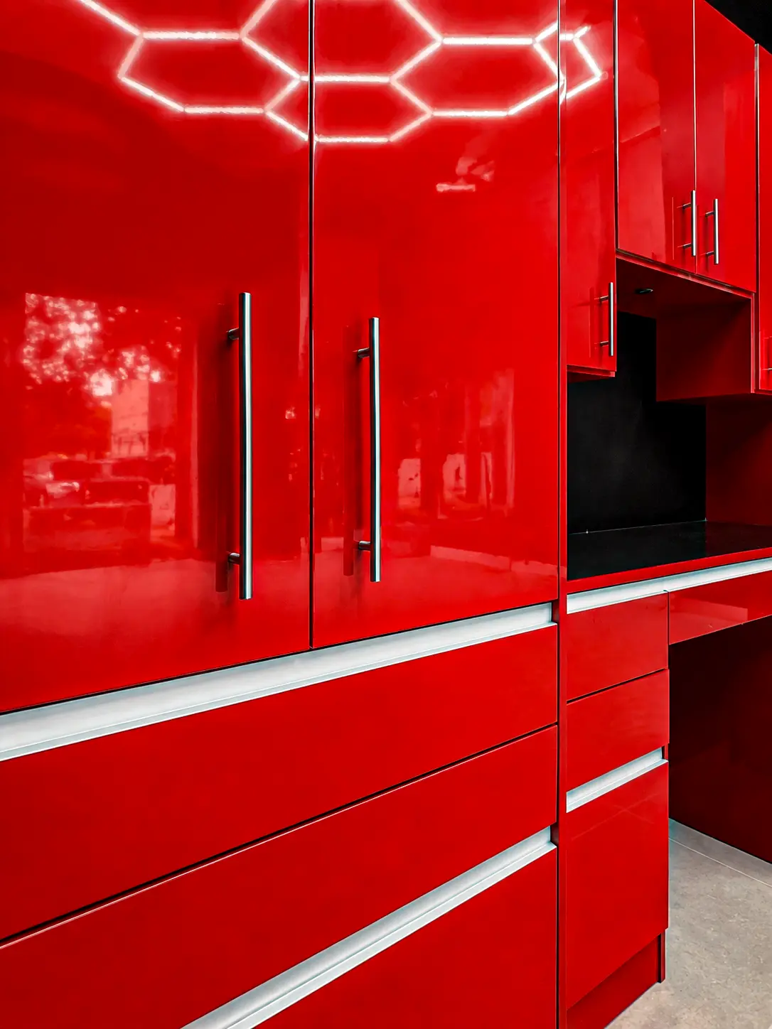 Close-up detail of glossy red garage cabinetry with silver bar handles, white accent stripes and reflected hexagonal LED ceiling lighting, designed by Custom Closet Florida