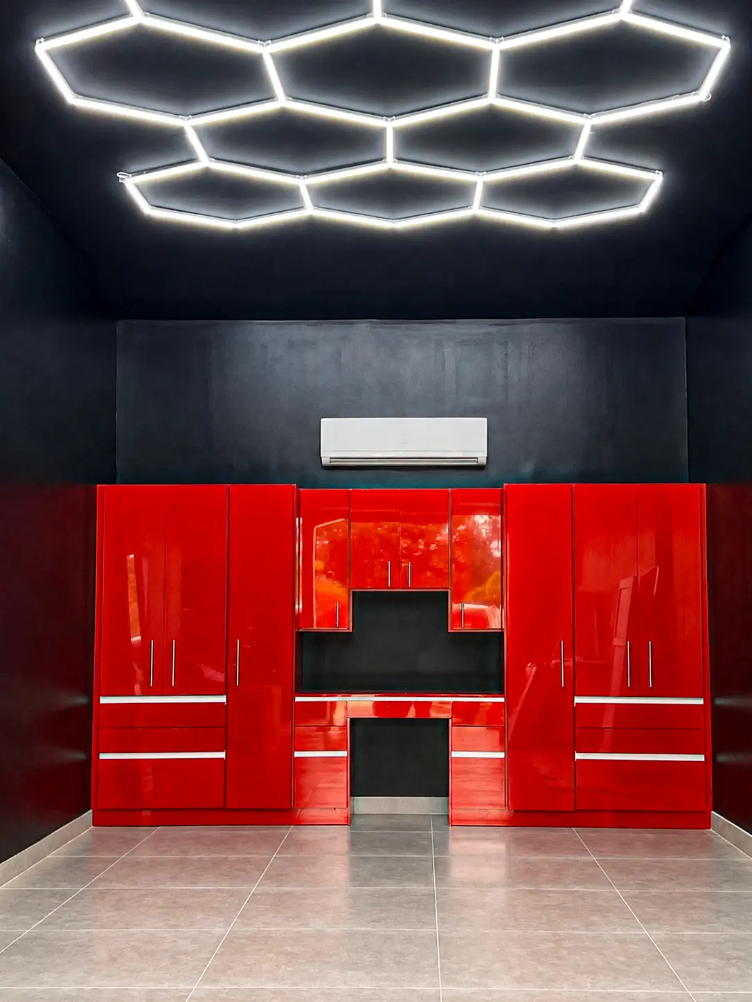 Full front view of a glossy red garage cabinet system with hexagonal LED ceiling lighting and built-in workbench, designed by Custom Closet Florida