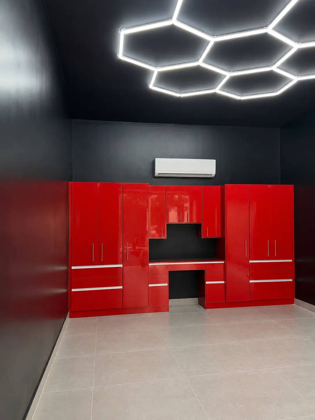 Glossy red garage cabinet system with a dramatic hexagonal LED ceiling design and built-in workbench area, designed by Custom Closet Florida