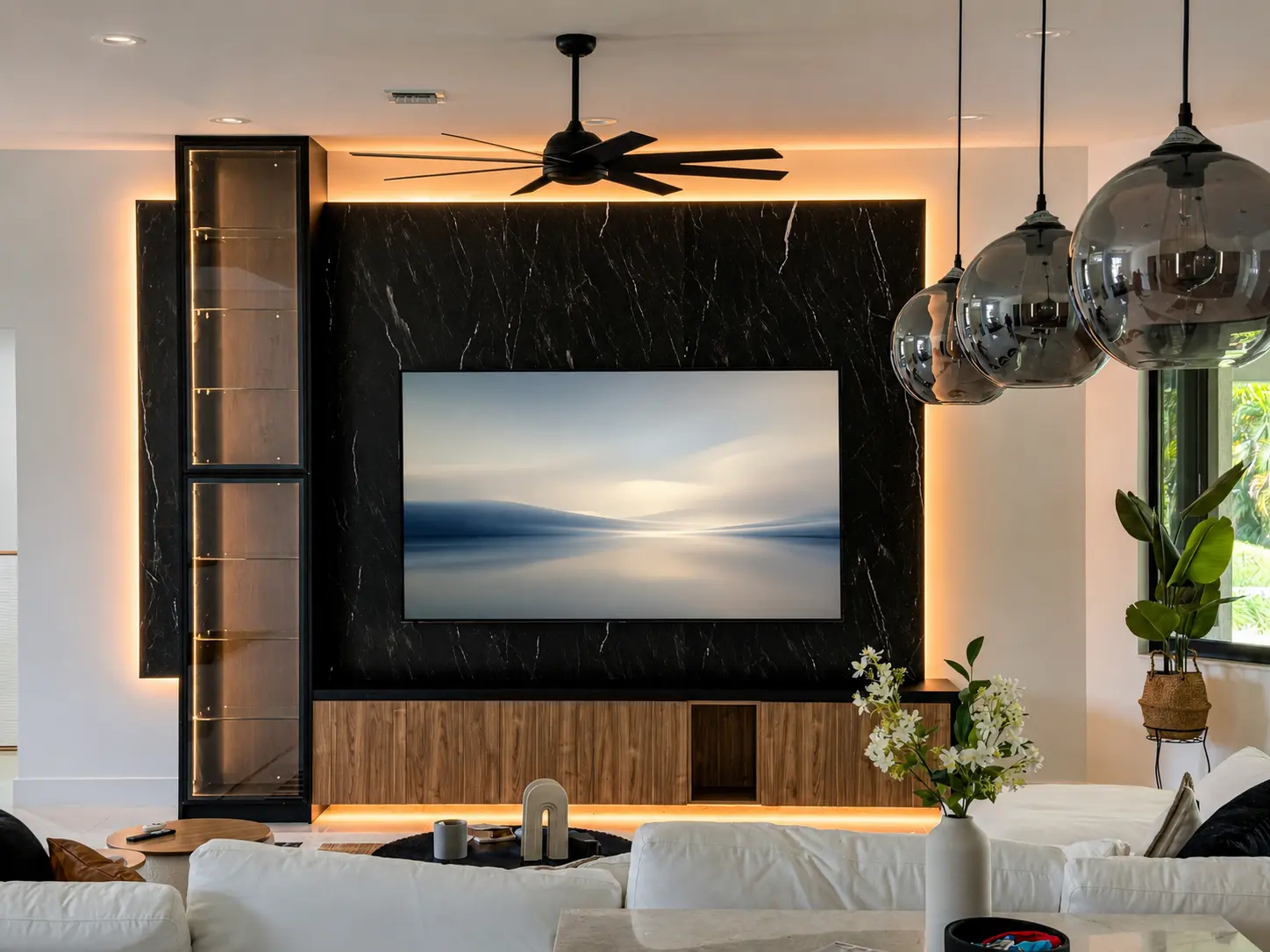 Custom entertainment center with black marble accent wall, glass display cabinet and wood console, designed and installed in a Parkland, FL living room by Custom Closet Florida